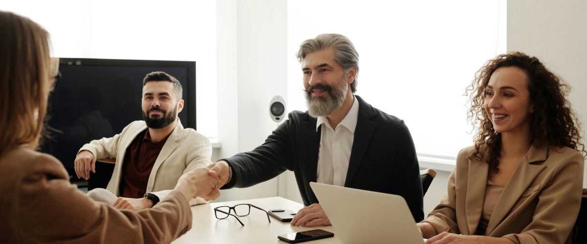 A group of business professionals shake hands during a meeting in a modern office setting.
